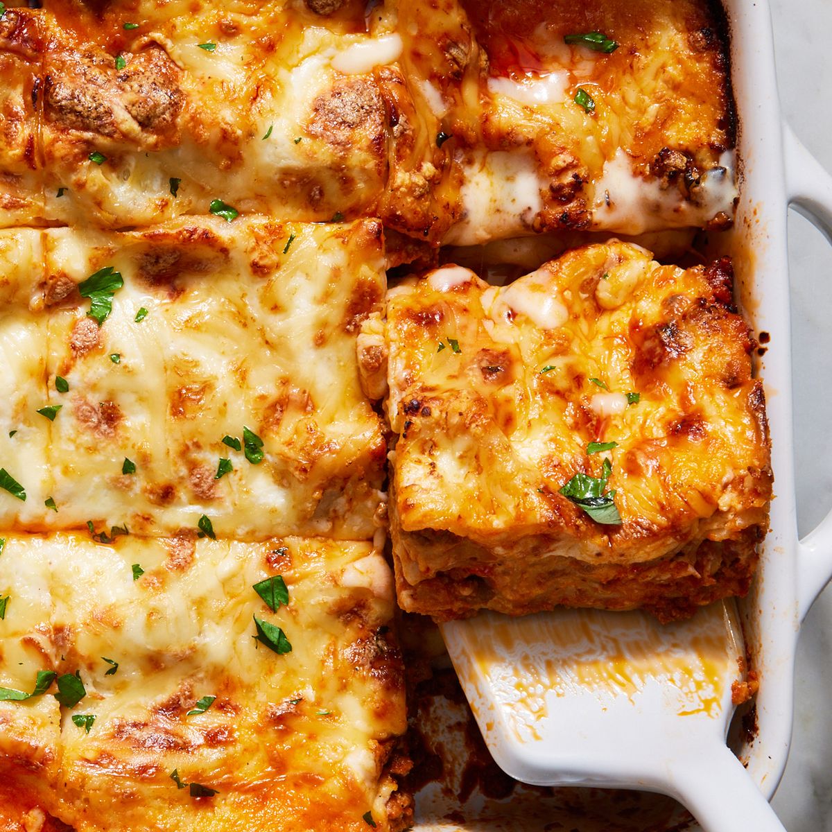 classic lasagna in a white pan topped with fresh herbs