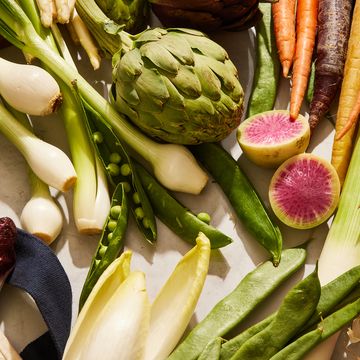 leeks, endive, artichokes, radishes, fava beans, peas, spinach, and carrots arranged on a marble surface