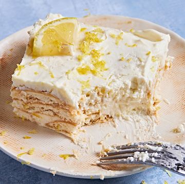 square slice of lemon icebox cake with a bite out on an off white plate on a blue background