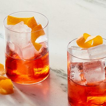 two glasses of negroni cocktails garnished with orange peels on a white marble background