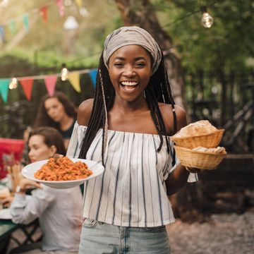 portrait of smiling young woman carrying food while standing in backyard during garden party