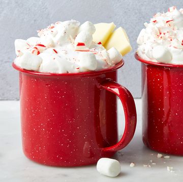 white hot chocolate in red mugs topped with whipped cream, crushed peppermint candies, white chocolate pieces, and mini marshmallows